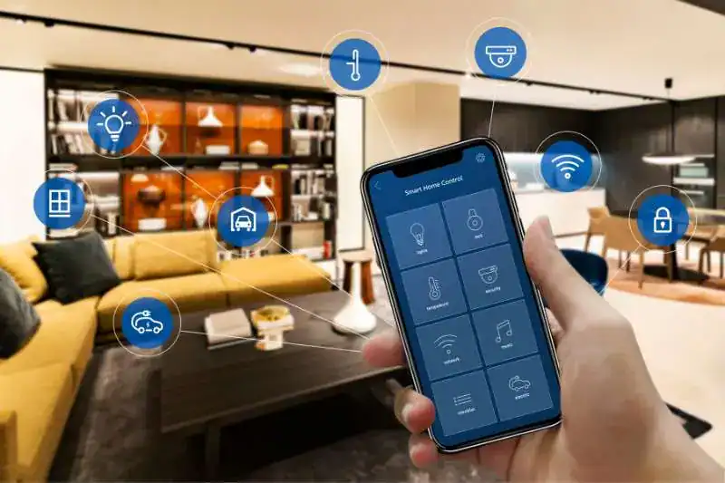 Osoba trzymająca smartfona z aplikacją do sterowania inteligentnym domem, z ikonami symbolizującymi różne urządzenia: światło, temperatura, monitoring, zamki, rolety, Wi-Fi, garaż, multimedia