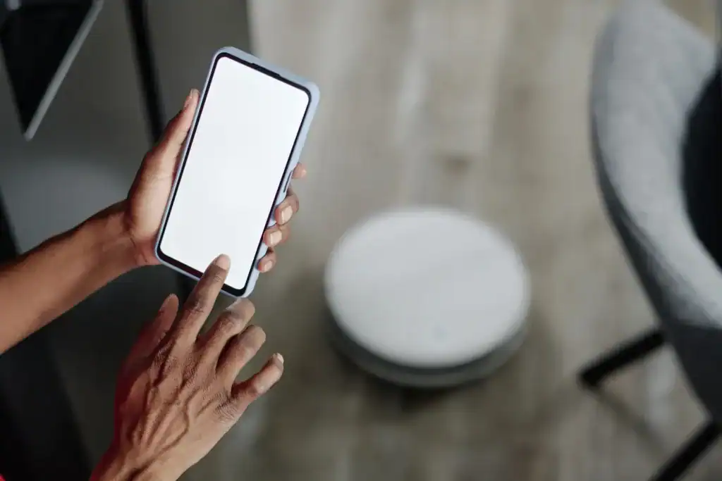 Osoba obsługująca aplikację mobilną na telefonie, kontrolując robota odkurzającego Dreame L20 Ultra, który znajduje się na podłodze.